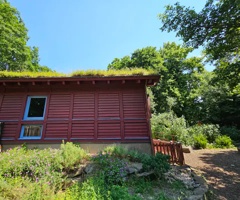 Die rote Fassade und das begrünte Dach des Hauses sind zu sehen.