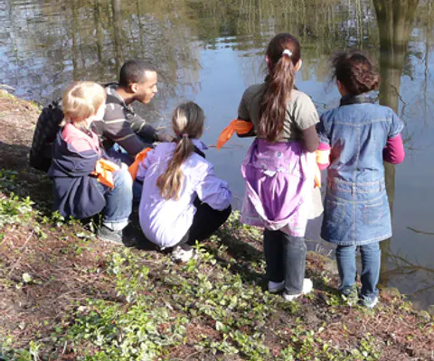Mehrere Kinder sitzen am Ufer und arbeiten mit Wasser und Eimern.