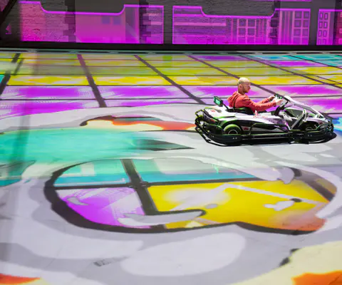 Ein Mann fährt mit einem E-Kart über eine bunt projizierte Hallenfläche.