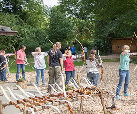 Mehrere Teilnehmende mit Bögen beim Bogenschießen im Freien.