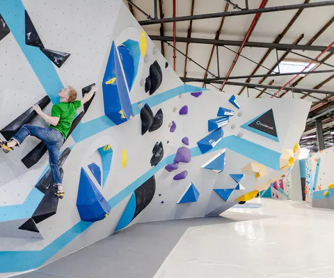 Eine Person klettert an einer farbigen Boulderwand in der Halle.