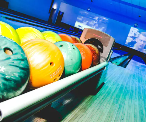 Bunte Bowlingkugeln liegen vor einer Bahn mit blauem Licht.