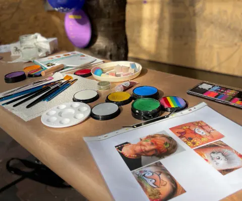 Auf einem Tisch liegen Schminkfarben, Pinsel und Vorlagen für fantasievolles Kinderschminken.