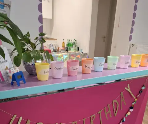 Ein pinker Tresen ist mit einer Happy-Birthday-Girlande und bunten Bechern dekoriert.