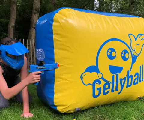 Ein Kind mit Schutzmaske zielt im Gras auf eine große gelb-blaue Gellyball-Station.
