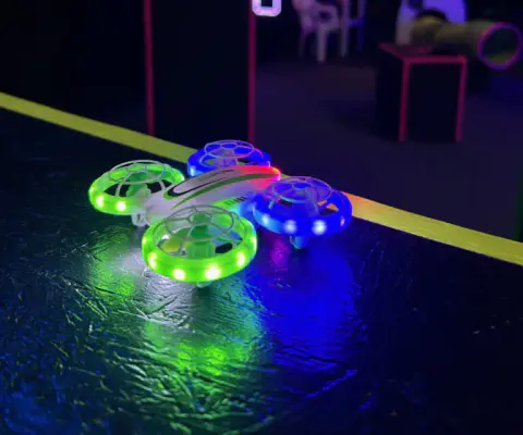 Ein kleiner leuchtender Spiel-Quadrocopter liegt auf einer dunklen Oberfläche.