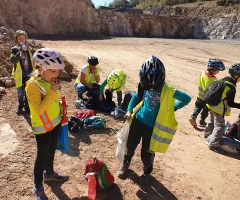 Mehrere Kinder mit Helmen und Warnwesten stehen auf offenem Steinbruchgelände.