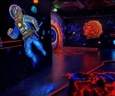 UV-beleuchteter Minigolfraum mit sichtbaren Bahnelementen und stimmungsvoller Atmosphäre.