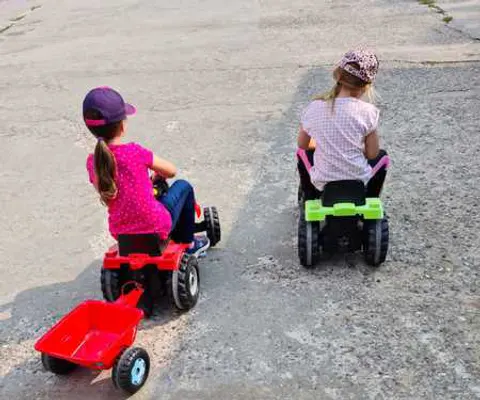 Zwei Kinder fahren mit Tretfahrzeugen über einen Hofweg.