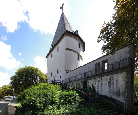 Der Adlerturm steht zwischen umliegenden Gebäuden und Bäumen.
