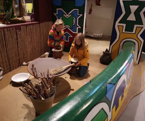 Zwei Kinder trommeln gemeinsam in einer spielerischen Museumsszene.