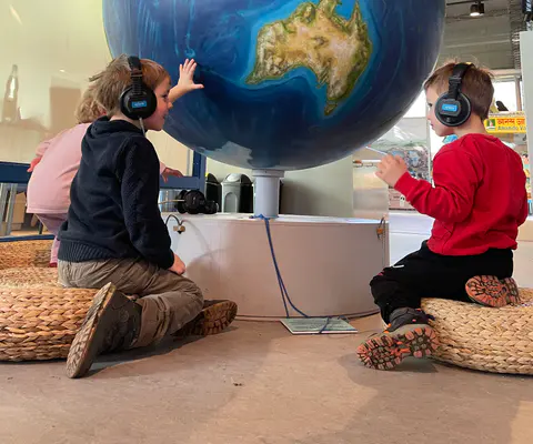 Kinder schauen staunend auf einen großen Globus im Museum.