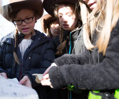 Mehrere Kinder mit Hüten betrachten gemeinsam etwas im Wald.