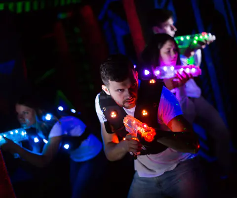 Drei Personen spielen Laser-Tag in einem dunklen Raum mit bunten Lichtern.