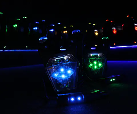 Mehrere beleuchtete Laser-Tag-Westen liegen in einem dunklen Raum nebeneinander.