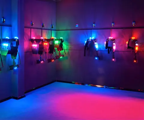 Mehrere beleuchtete Laser-Tag-Westen hängen an den Wänden eines dunklen Raums.