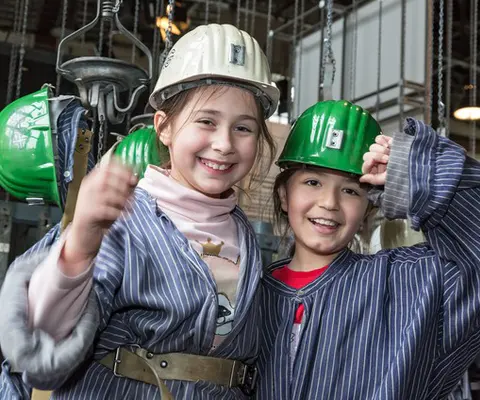 Zwei Kinder mit Schutzhelm und Grubenhemd stehen zusammen.