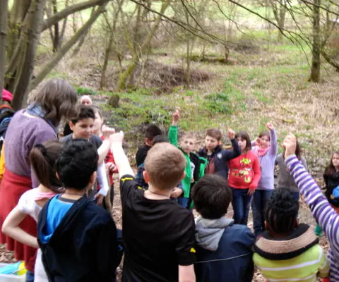 Eine Gruppe Kinder steht im Wald mit erhobenen Armen im Kreis.