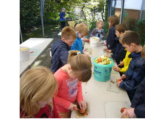 Kinder schneiden an langen Tischen draußen Obst und Gemüse.