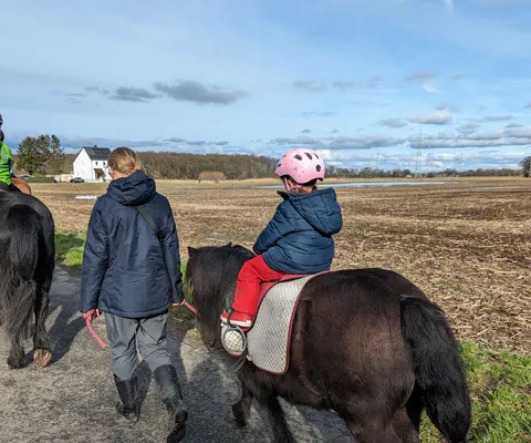 Ein Kind reitet mit Begleitung auf einem Pony im Freien