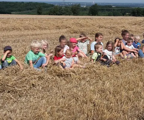 Eine Gruppe von Kindern sitzt auf einem Strohberg auf einem abgeernteten Feld.