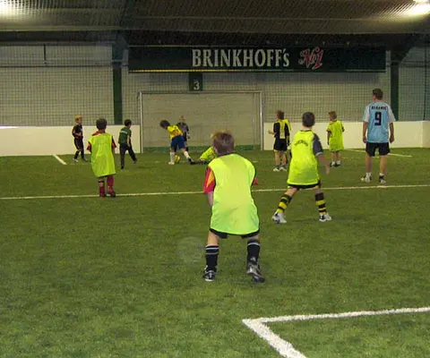 Mehrere Kinder spielen Fußball in der Halle vor dem Tor.