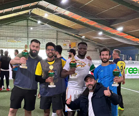 Eine Gruppe posiert mit Pokalen auf dem Spielfeld.