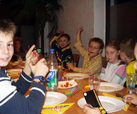 Kinder sitzen an einem gedeckten Tisch in der Geburtstagsrunde.