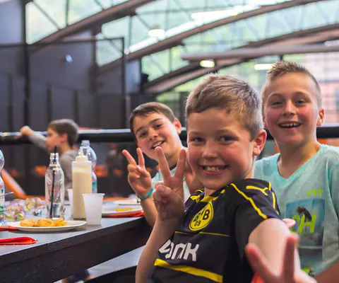 Mehrere Jungen sitzen lächelnd an einem Tisch und zeigen das Peace-Zeichen.