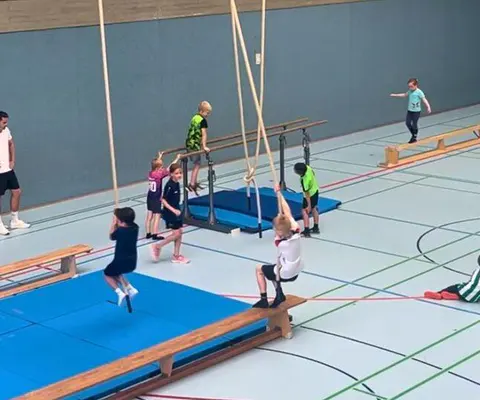 Mehrere Kinder bewegen sich mit Sportgeräten in der Halle.