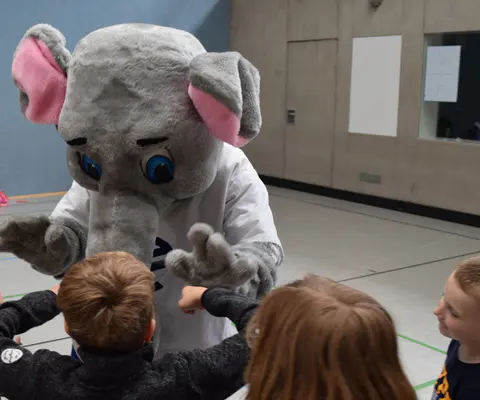 Ein Maskottchen steht mit Kindern in der Halle.