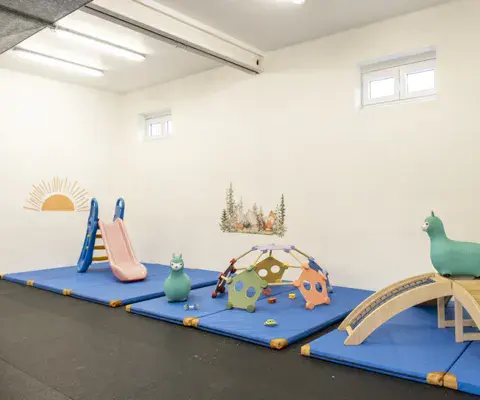 Ein heller Turnraum mit Matten, kleinen Kletterelementen und Spielfiguren.